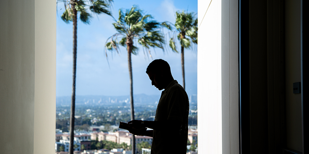 An individual in shadow, standing in front of window with Playa Vista and palm trees in the background.